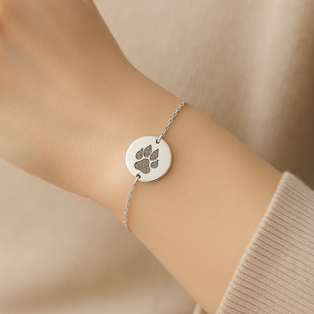 Silver bracelet with a paw print charm on a wrist against a beige background