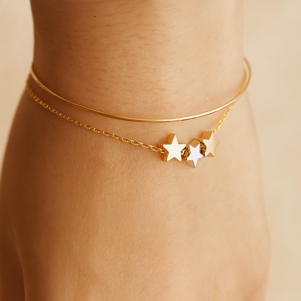 Gold bracelet with 3 star charms on a person's wrist against a beige background