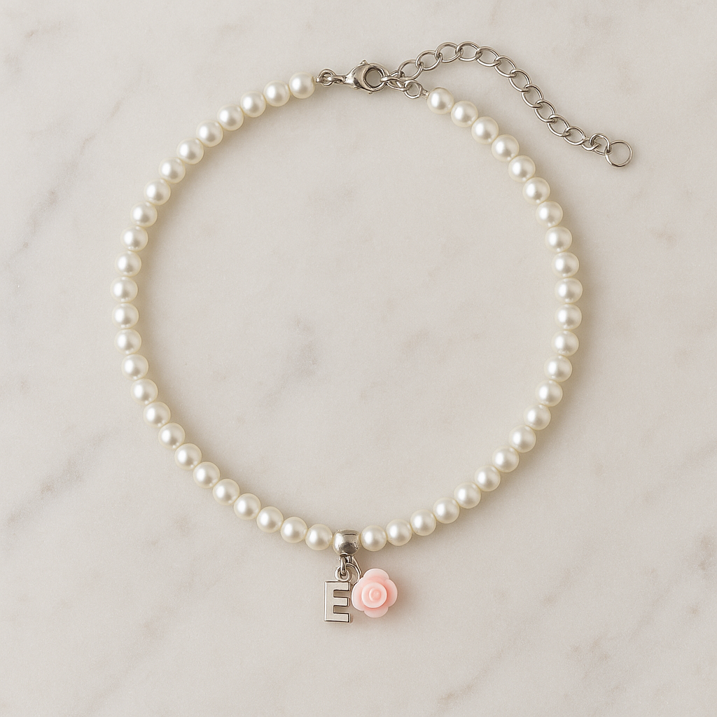 Pearl necklace with a pink rose charm and silver 'E' on a marble background